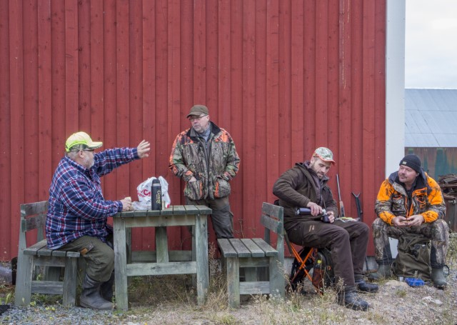 Fyra män i jaktkläder sitter ner och dricker kaffe